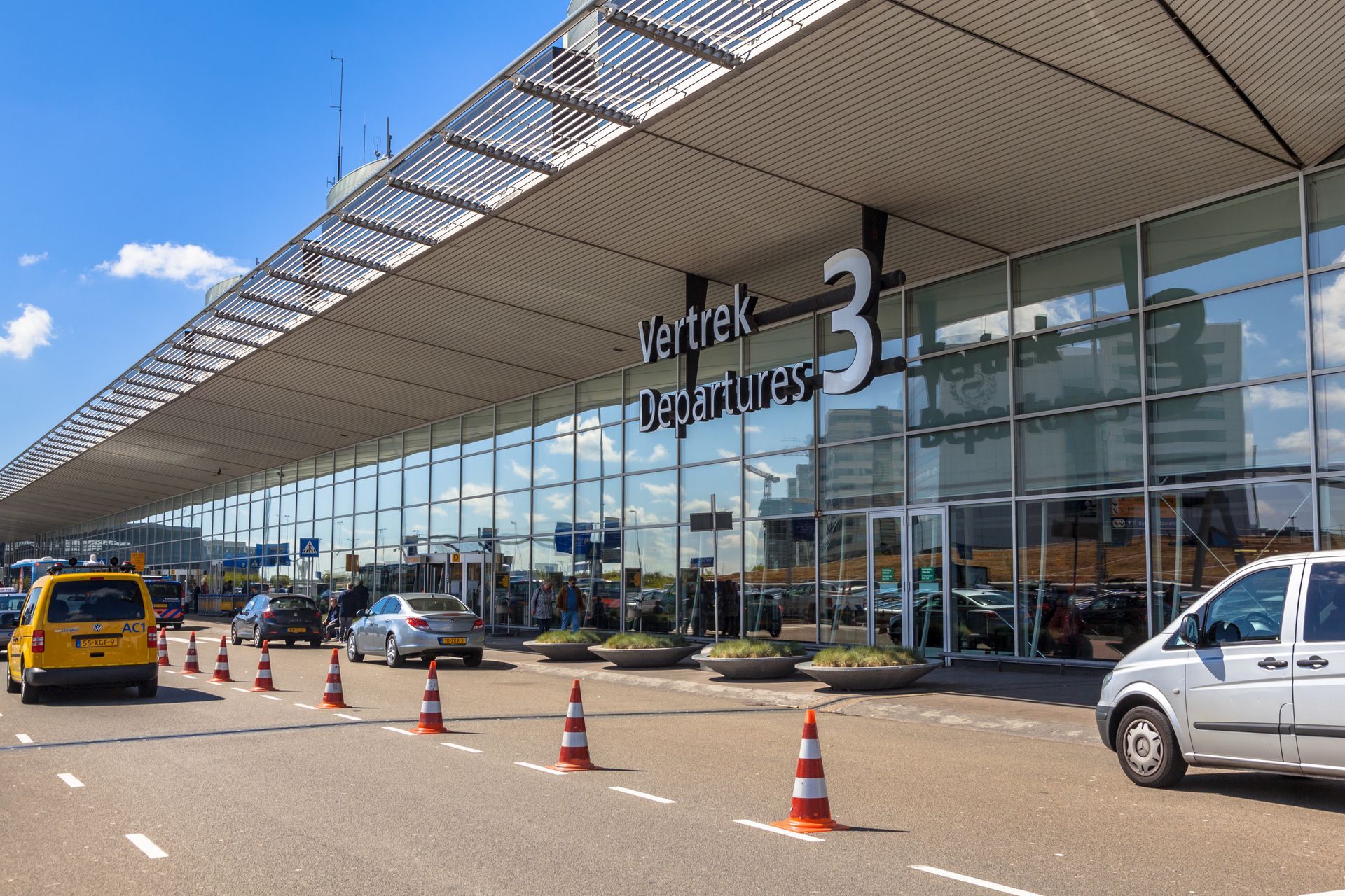 Voor een groot gebouw staat een wit busje geparkeerd.