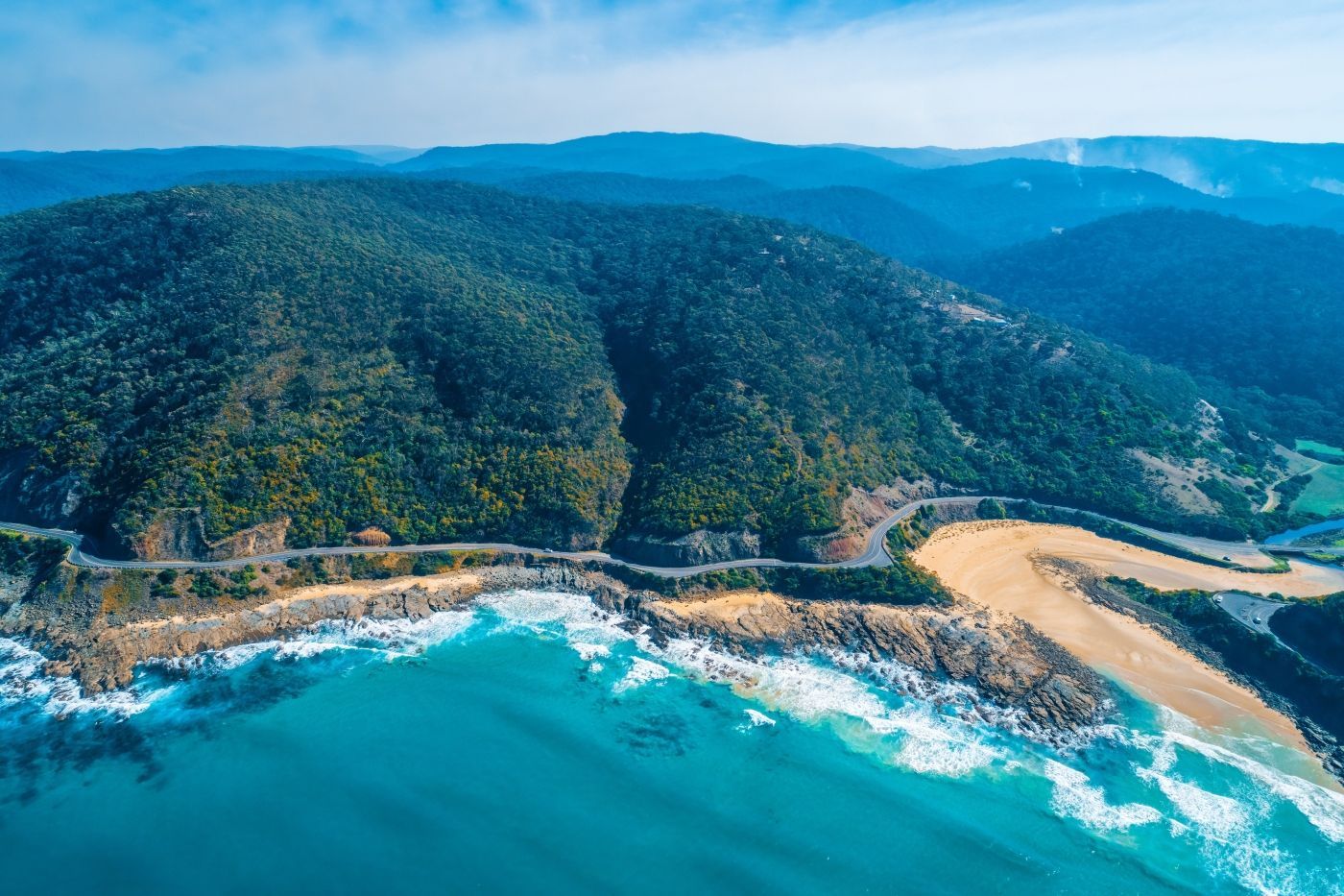 Een luchtfoto van een strand omgeven door bergen en bomen.