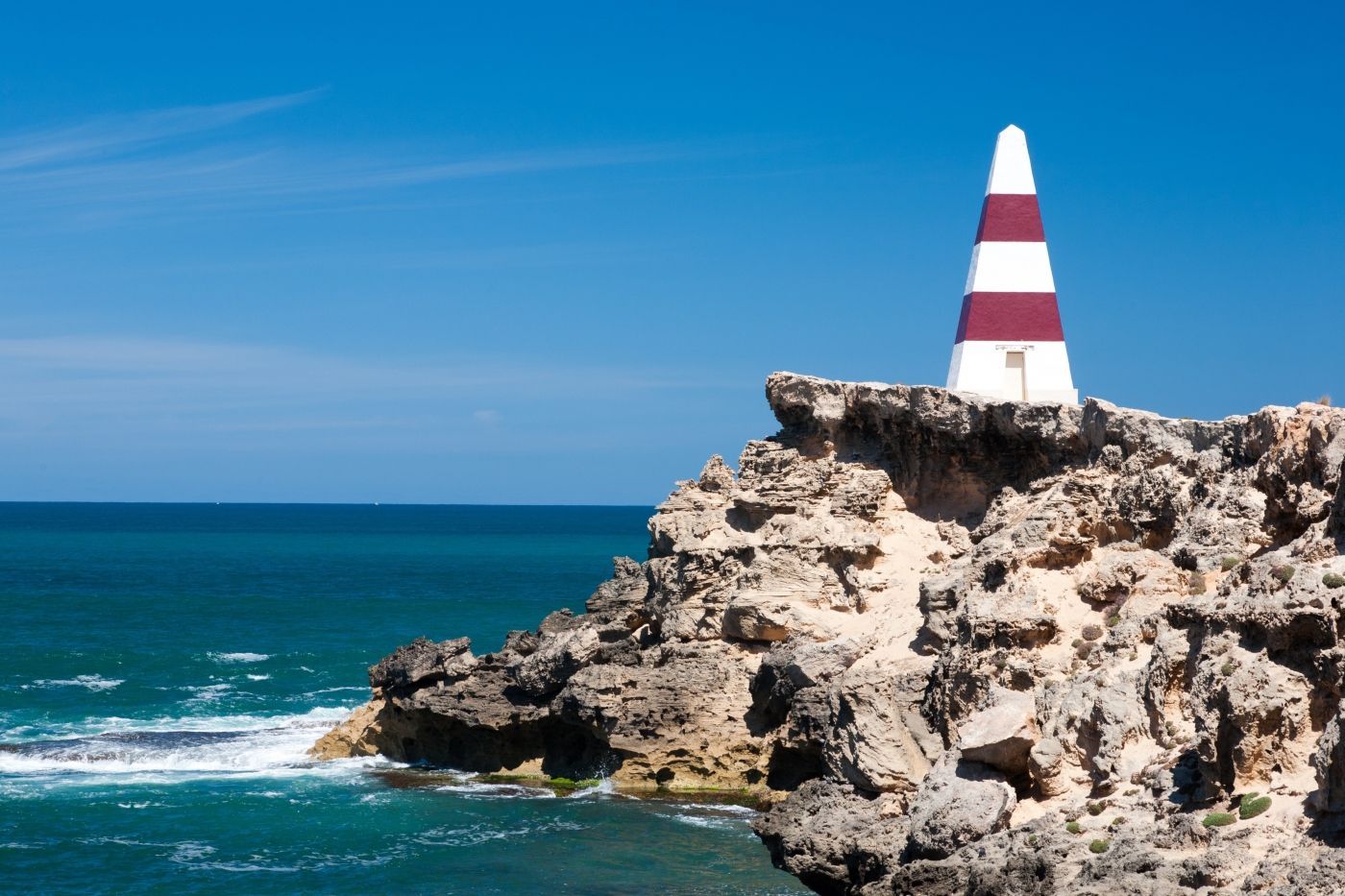 Een rood-witte vuurtoren op een rotsachtige klif met uitzicht op de oceaan