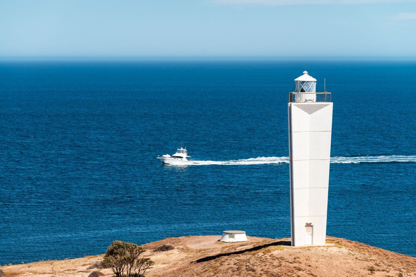 Een vuurtoren op een heuvel met uitzicht op de oceaan met een boot in de verte.