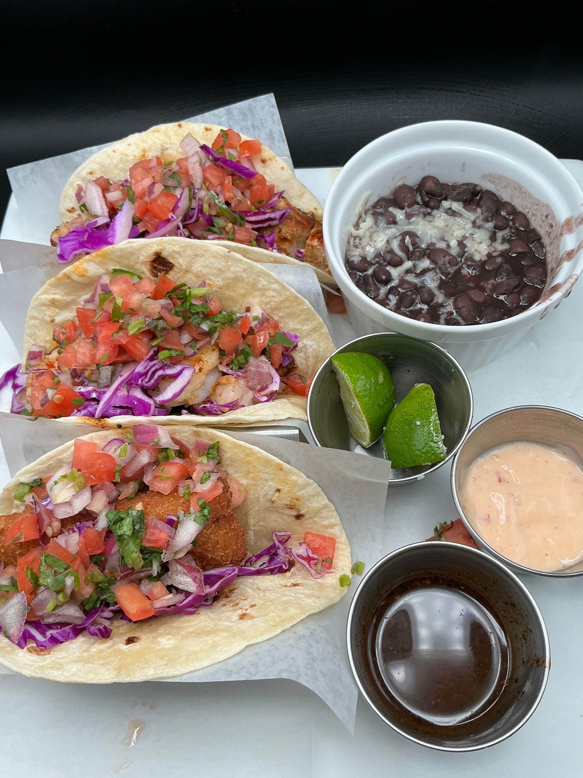 Three fish tacos with salsa, black beans, lime, and sauce.