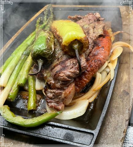 Sizzling steak and grilled vegetables (asparagus, peppers, onions) on a hot cast iron plate.