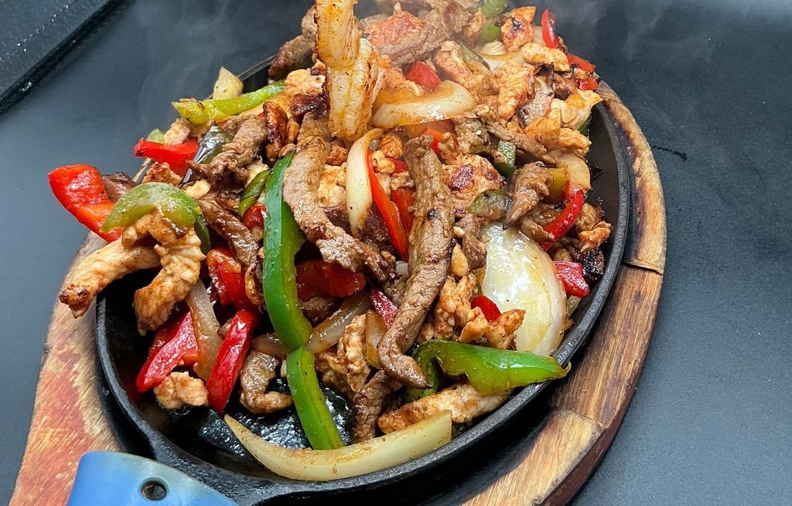 Sizzling fajitas on a hot skillet, with steak, shrimp, peppers, and onions.