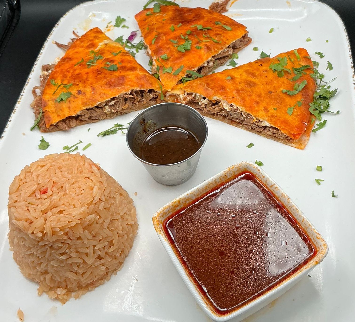 Birria quesadillas with dipping sauces and rice on a white plate.