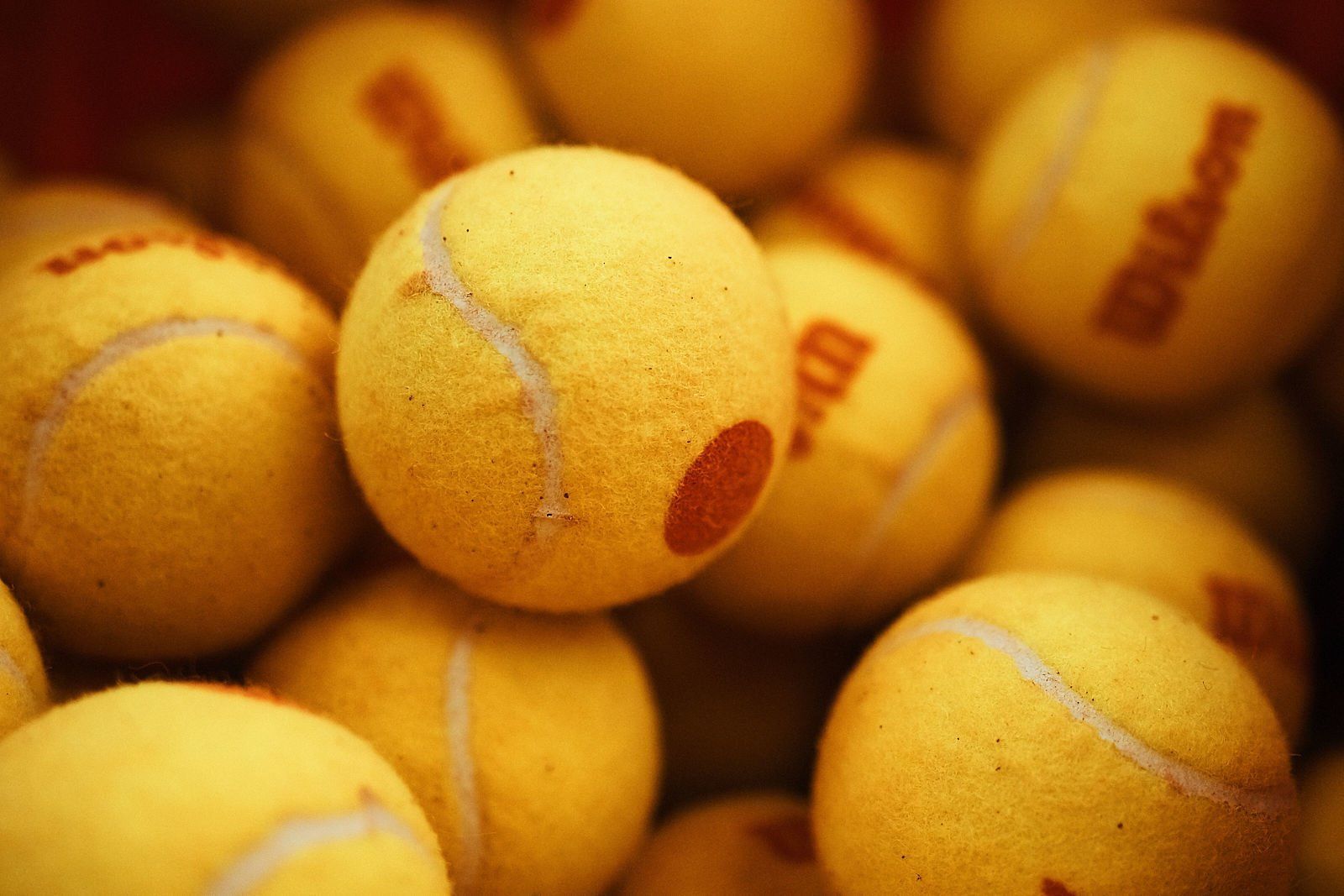 Pilha de bolas de tênis amarelas, algumas com o logotipo da Wilson visível.