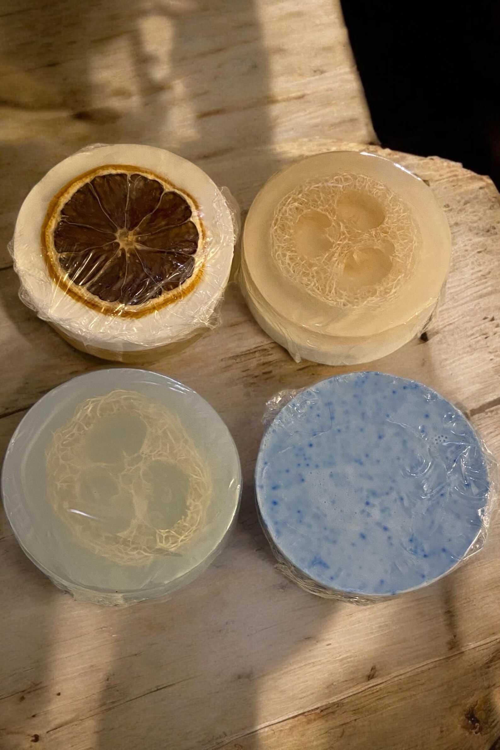 Four soaps are stacked on top of each other on a wooden table.