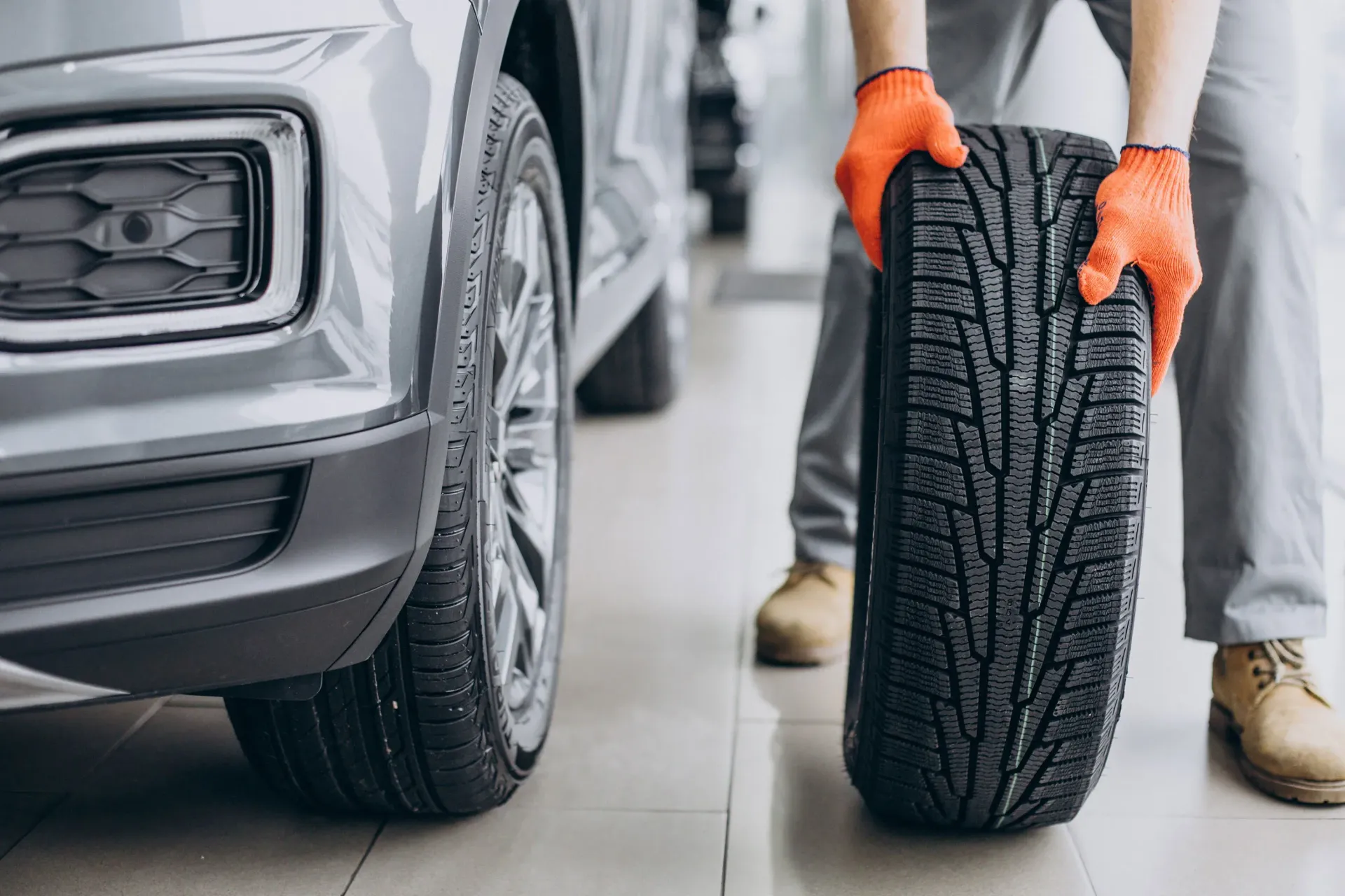 A man is holding a tire in front of a car.