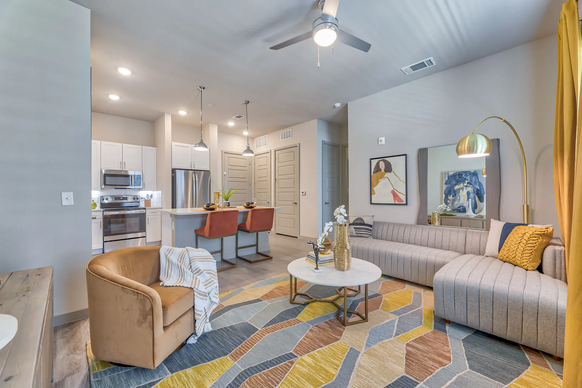 Open-concept living area with a kitchen island, stainless-steel appliances, and a gray sofa.