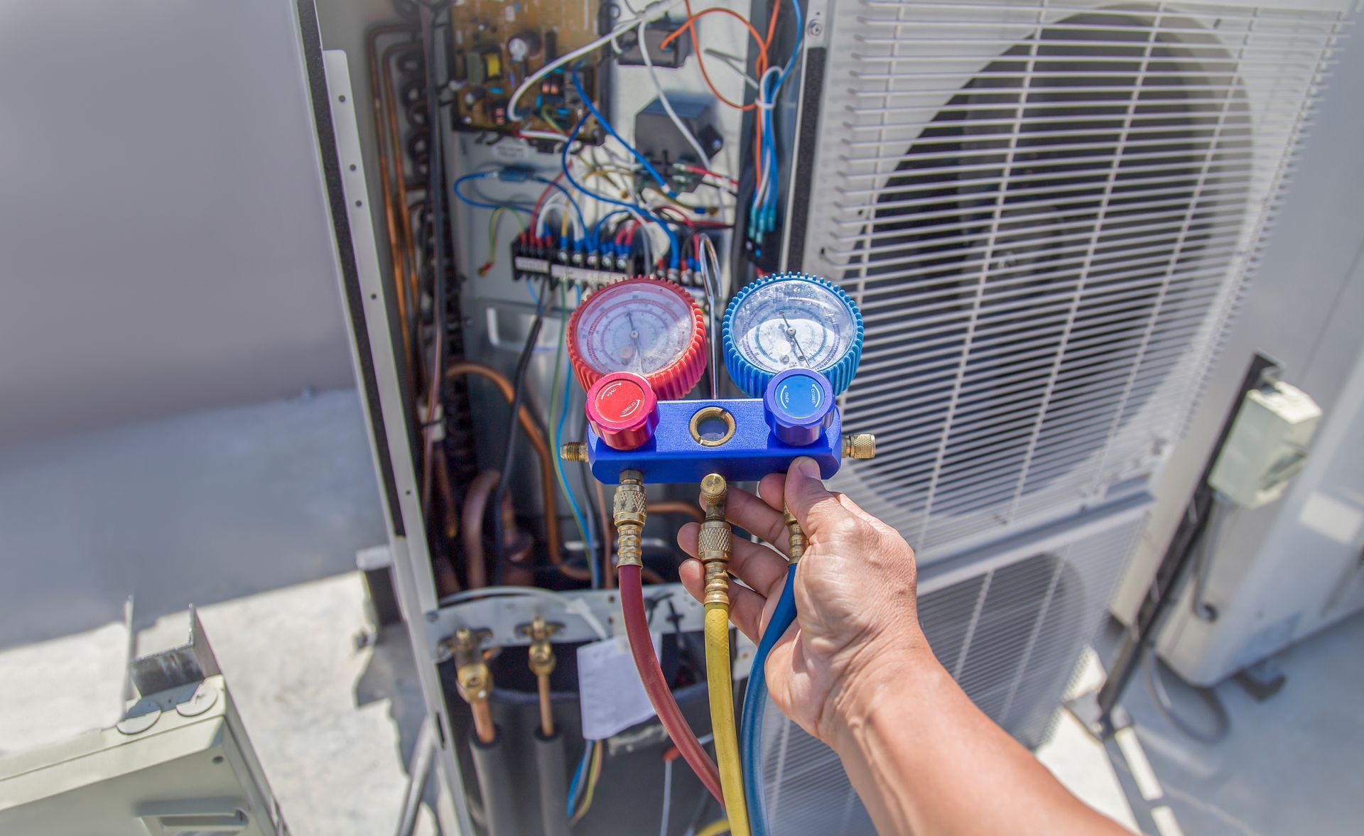 HVAC technician using gauges to service an air conditioning unit outdoors.