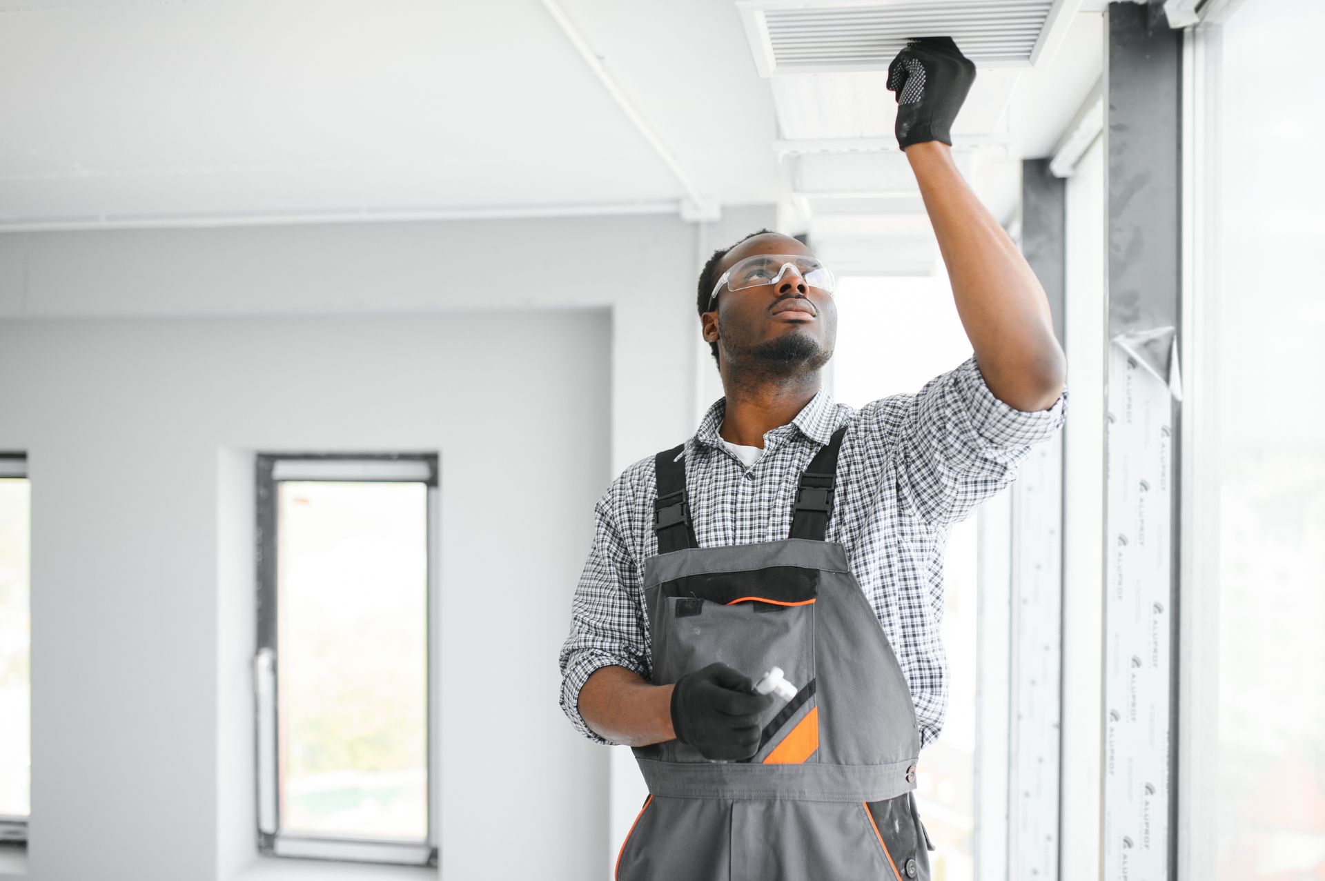 Person cleaning a ceiling air vent with a long, rotating brush.