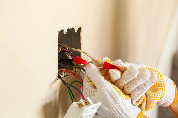 Hands in gloves wiring electrical outlet in a wall.