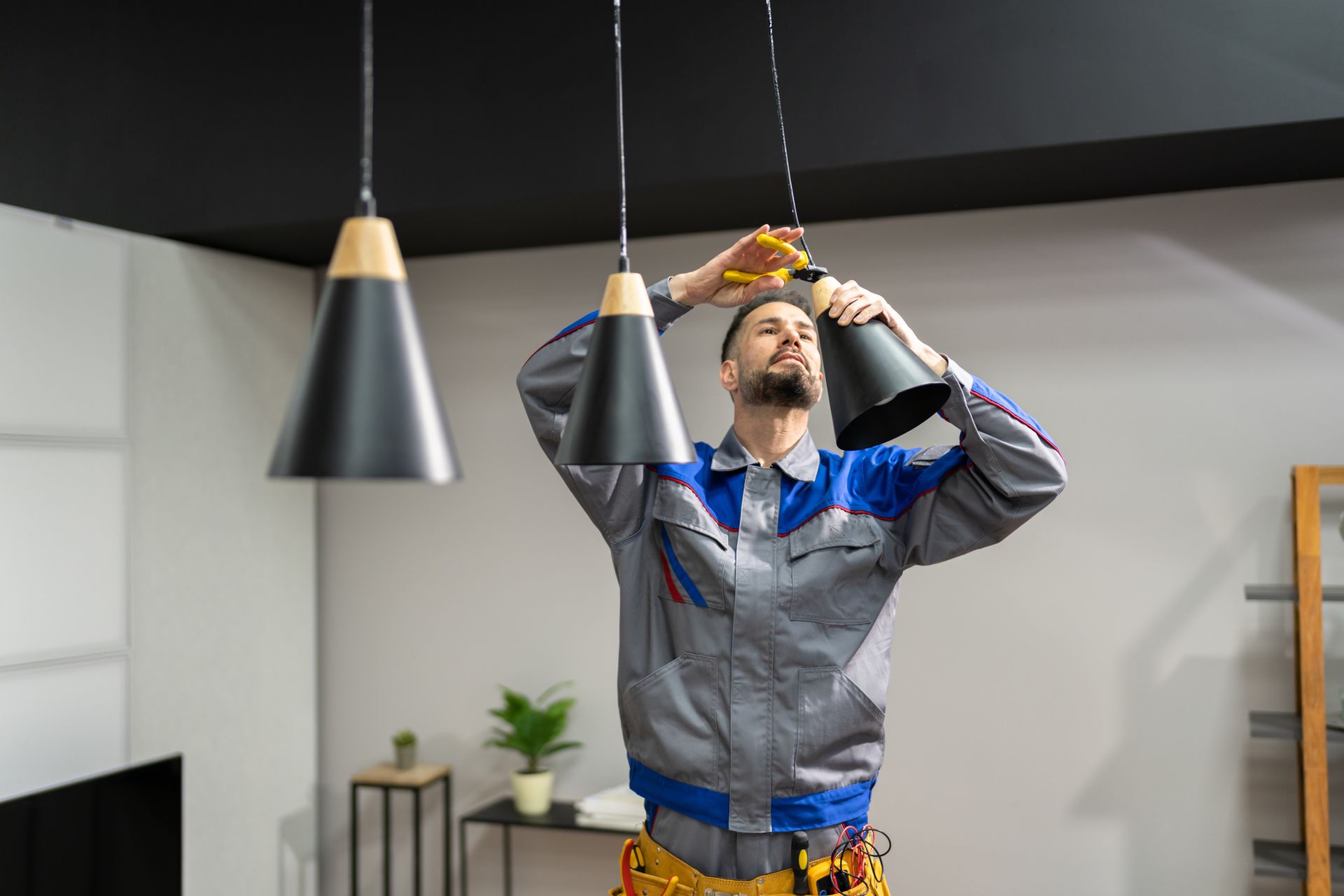 Man in work clothes installing a pendant light fixture on a black ceiling.