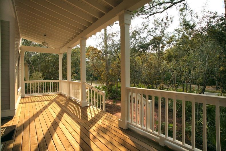 Sunlit wooden porch with white railings overlooking trees and a yard
