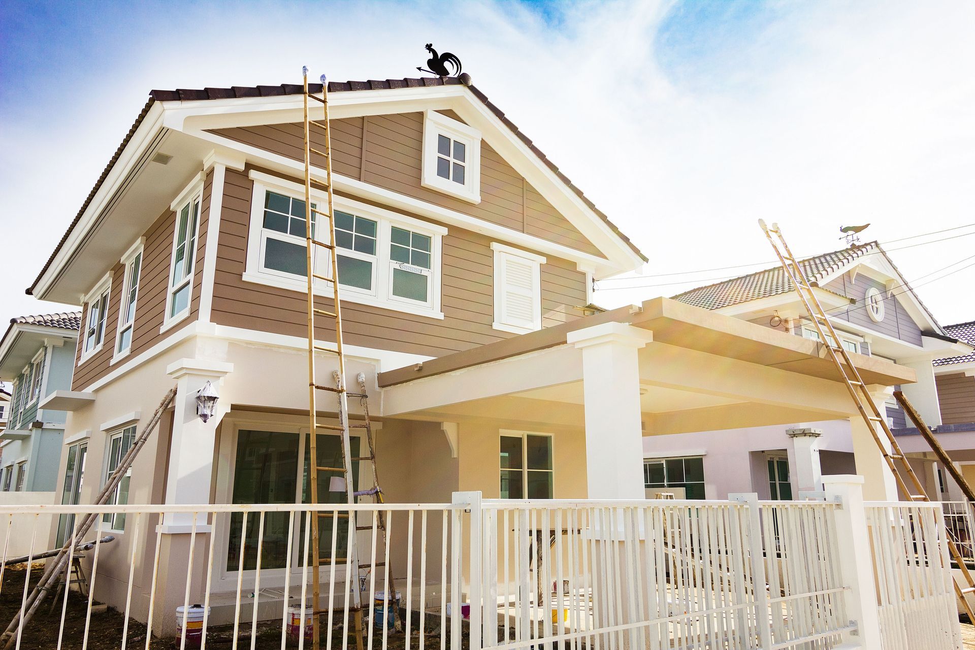 Two-story beige house with white trim, front porch, and a white fence in bright daylight