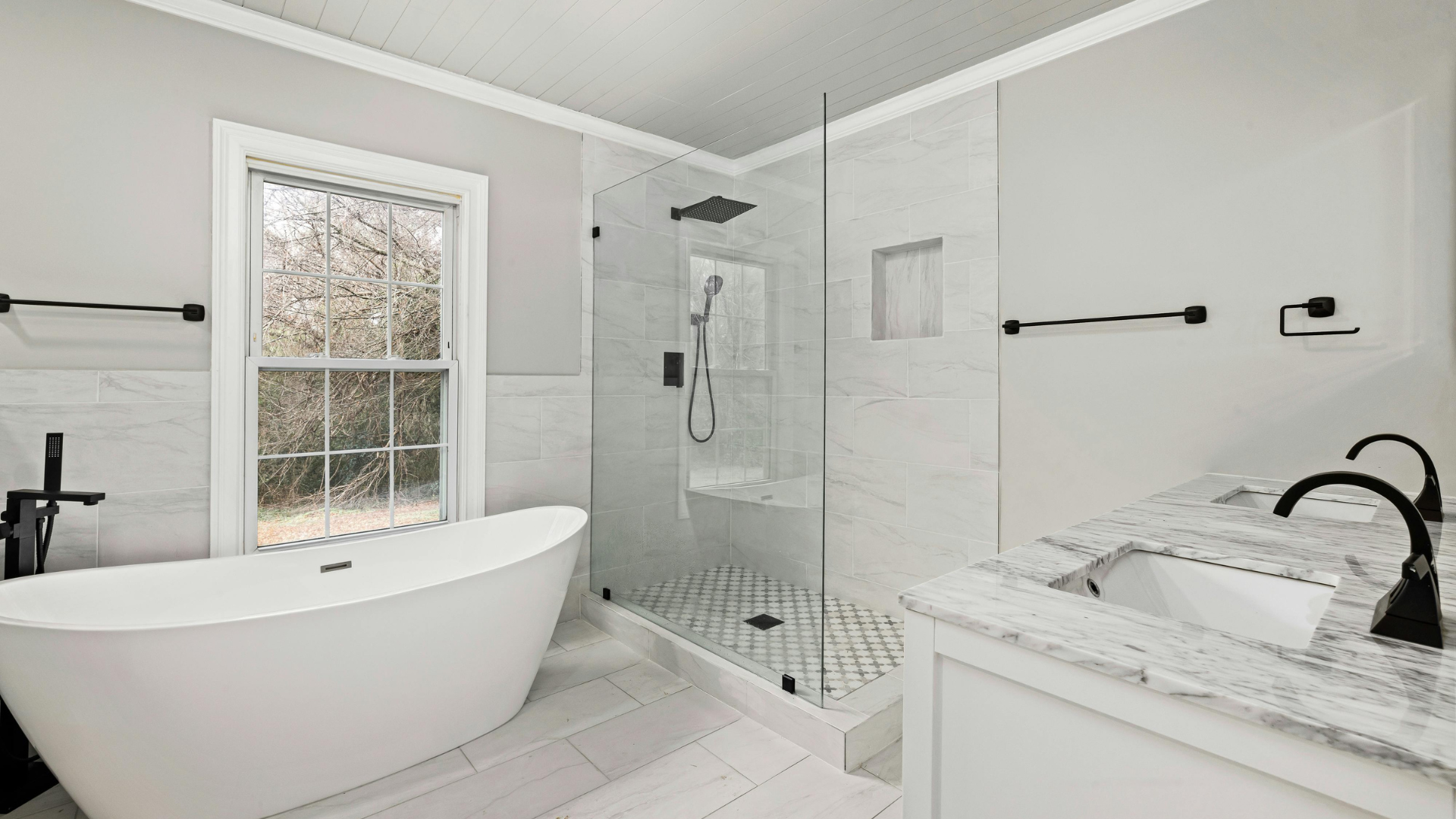 Bright modern bathroom with freestanding tub, glass shower, and white vanity by a window