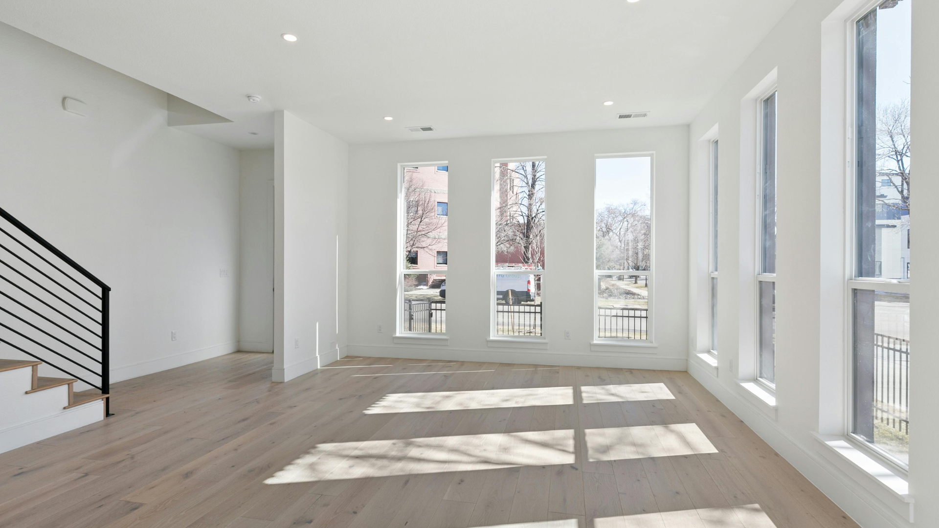 Bright empty modern living room with white walls, wood floors, and large sunlit windows