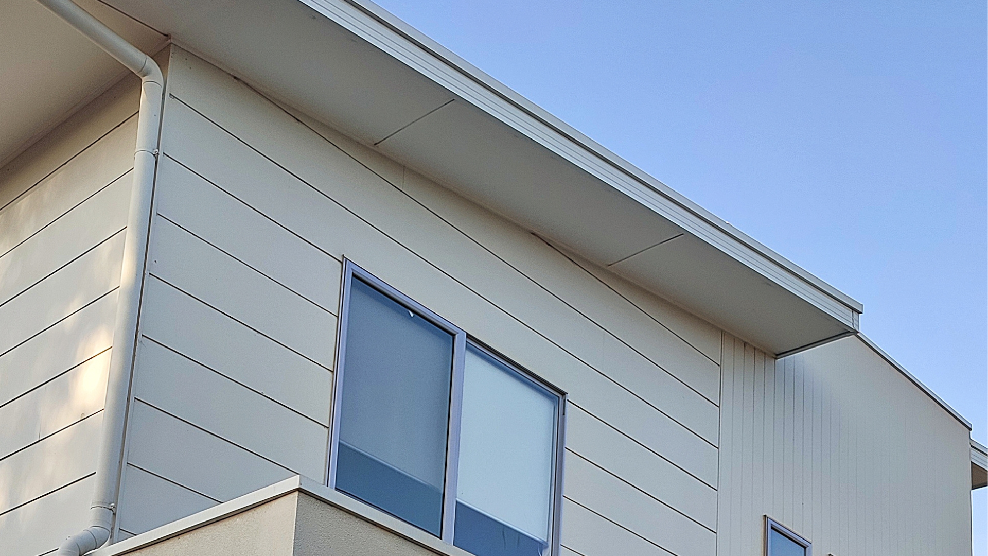 Corner of a light beige house with white trim and a blue sky above