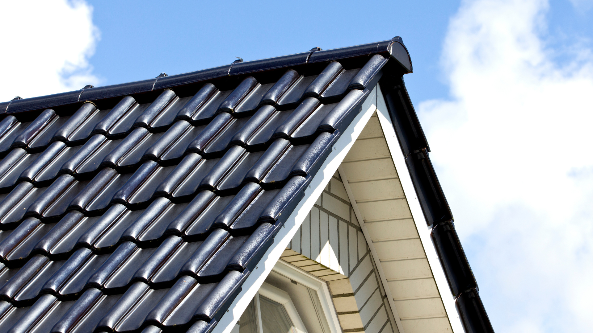 Black tiled roof edge against a bright blue sky with clouds