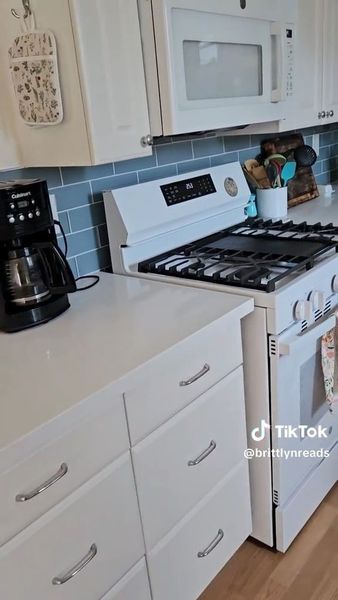 Bright white kitchen with a stove, coffee maker, microwave, and countertop appliances.