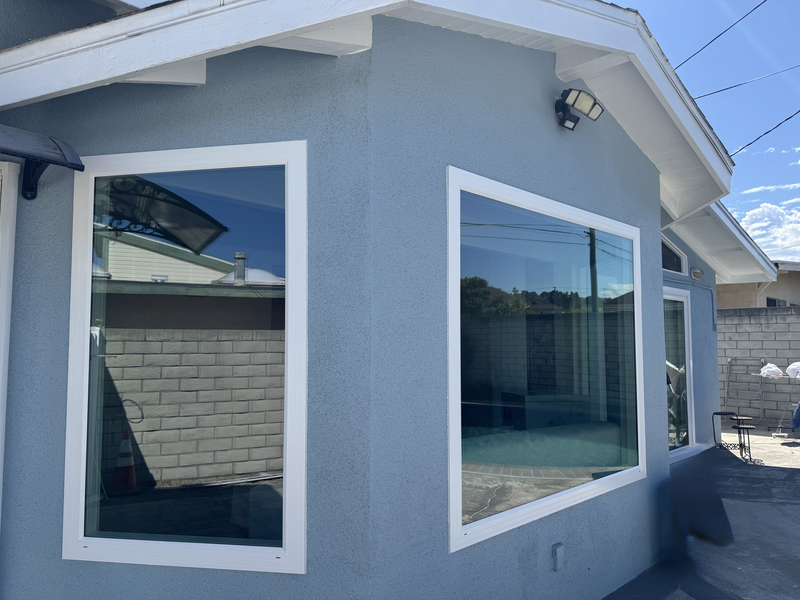 Gray house exterior with two large windows and white trim under a sloped roof