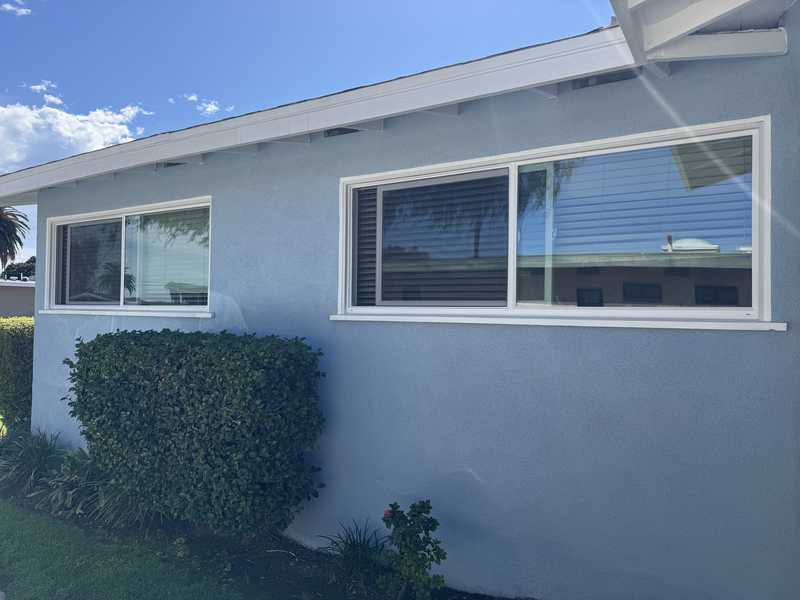 Exterior of a light gray house with white-framed windows and a trimmed hedge in front