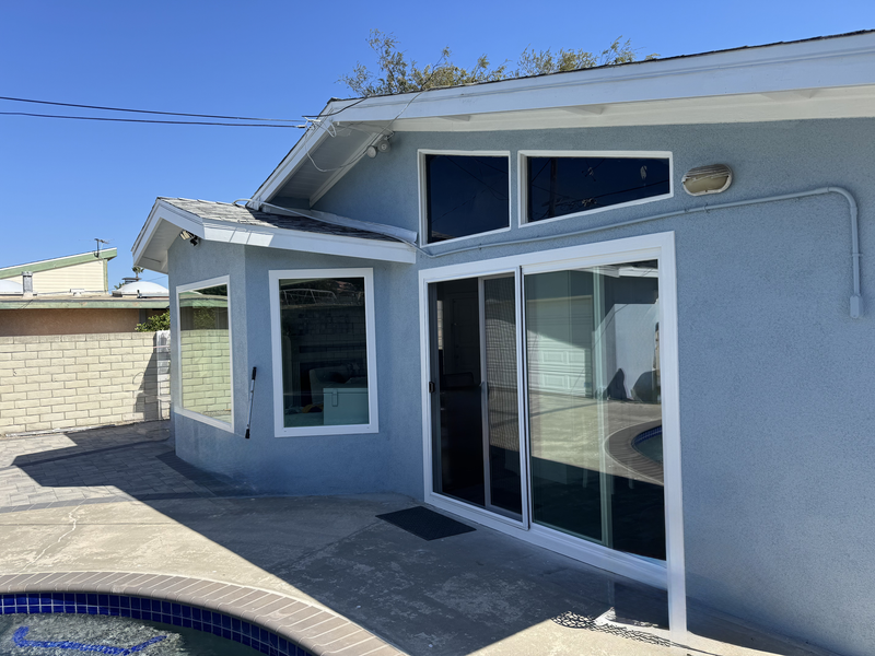 Back patio of a stucco house with sliding glass doors and a small covered window nook under a blue sky