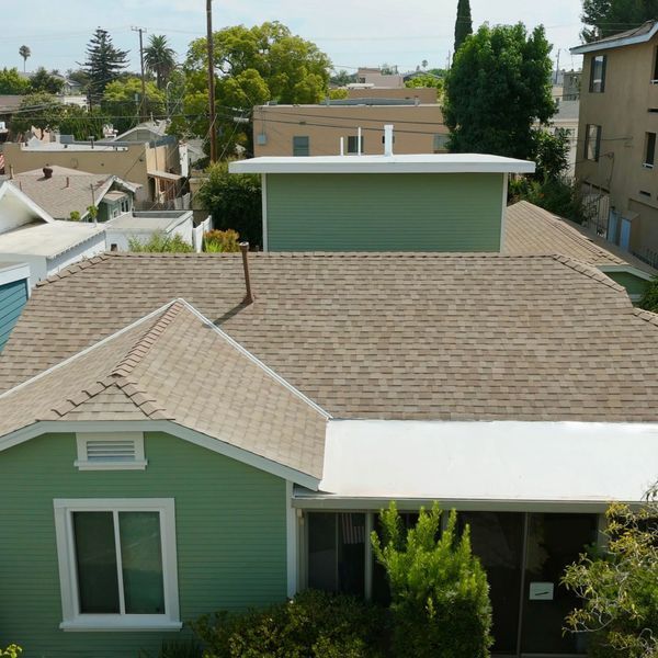 Aerial view of a green house with beige roof in a residential neighborhood.