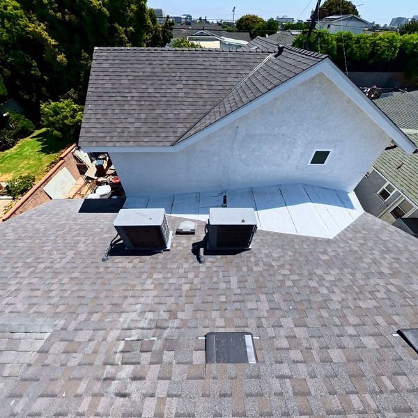 Rooftop with gray shingles, two HVAC units, and a white chimney-like structure under a clear sky