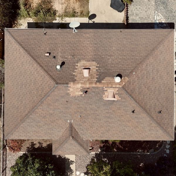 Aerial view of a tan shingled house roof with several vents and a satellite dish