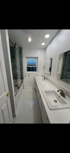 Modern white bathroom with double sink vanity, large mirror, and window at the far end.