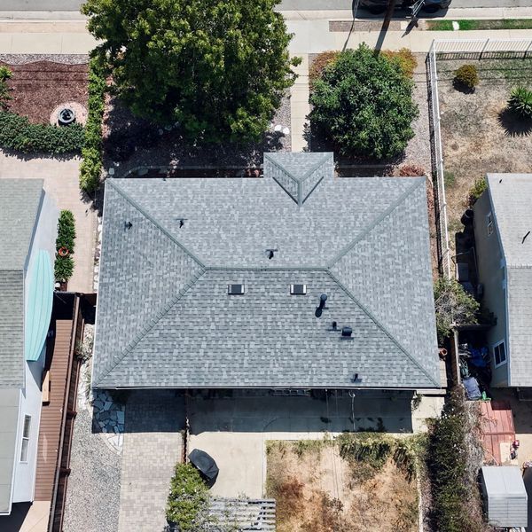 Aerial view of a single-story house with a gray roof, driveway, and small front yard.