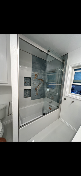 Modern bathroom with a glass-enclosed bathtub, gray tile shower wall, and small window.