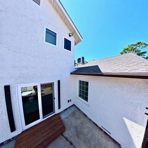 Backyard patio between white stucco house walls with sliding glass doors and a small deck.