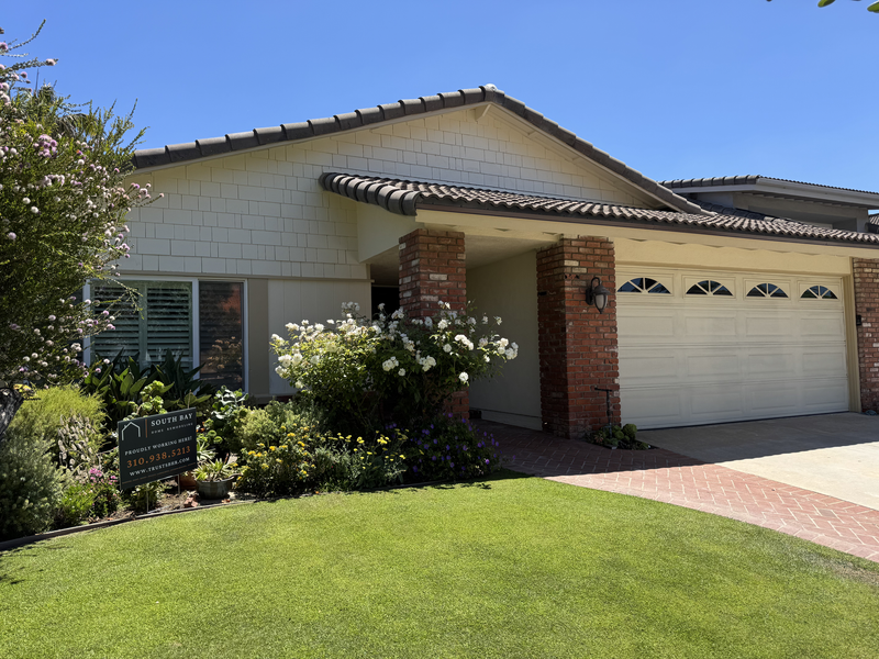 Single-story suburban house with a brick entry, two-car garage, and green front lawn in bright sunlight