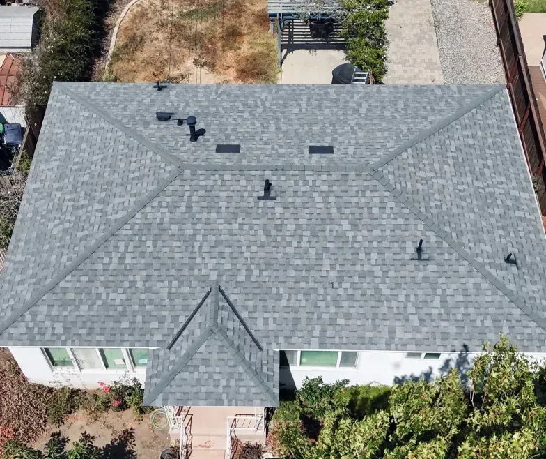 Aerial view of a house with a gray shingled roof, front walkway, and surrounding trees.