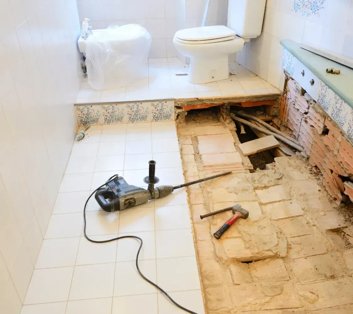 Bathroom under renovation with removed bathtub, exposed floor, and tools on the tiles