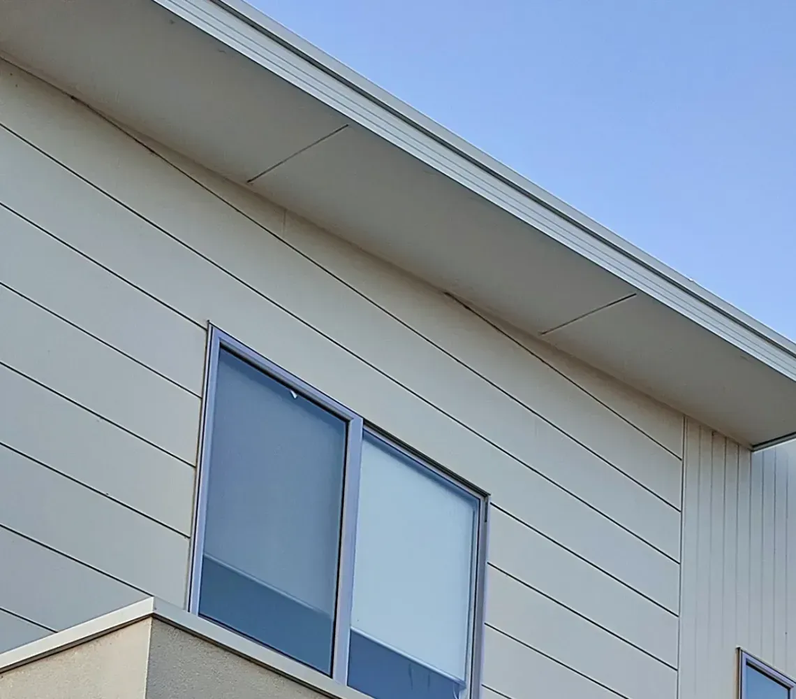 Side of a beige house with white trim and two second-story windows against a blue sky