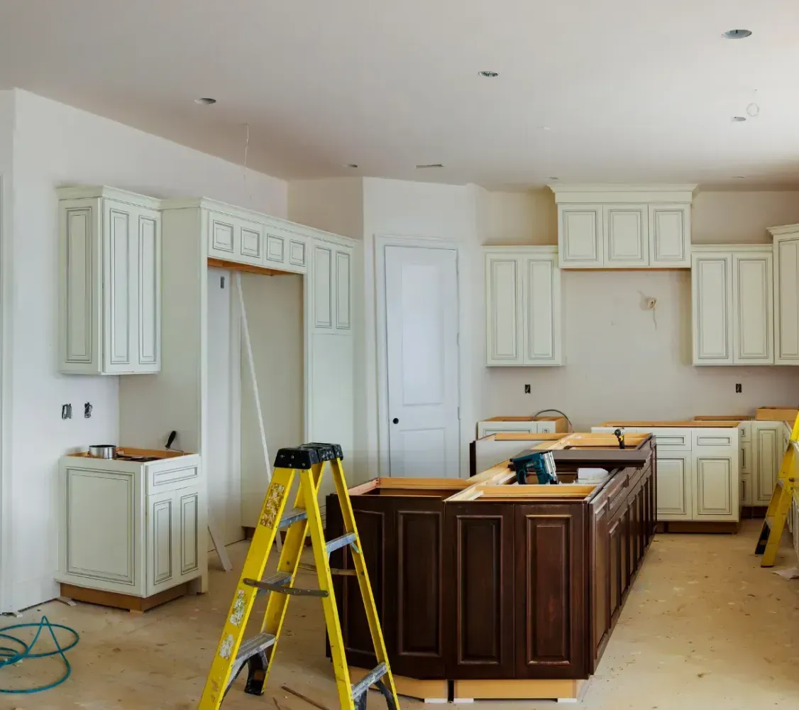Kitchen under renovation with white cabinets, an island, and a yellow ladder on unfinished flooring