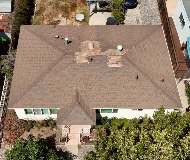 Aerial view of a tan-roofed house with surrounding trees and neighboring homes.