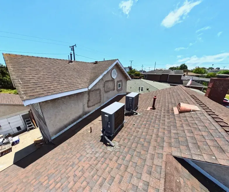 Rooftop with brown shingles, vents, and chimneys under a bright blue sky