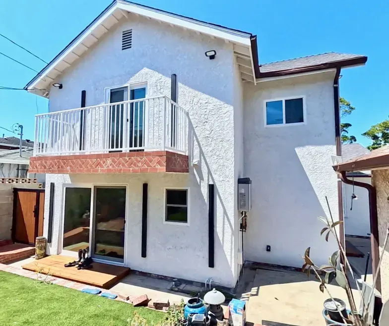 Two-story white house with balcony, red tile roof, and small lawn under a bright blue sky