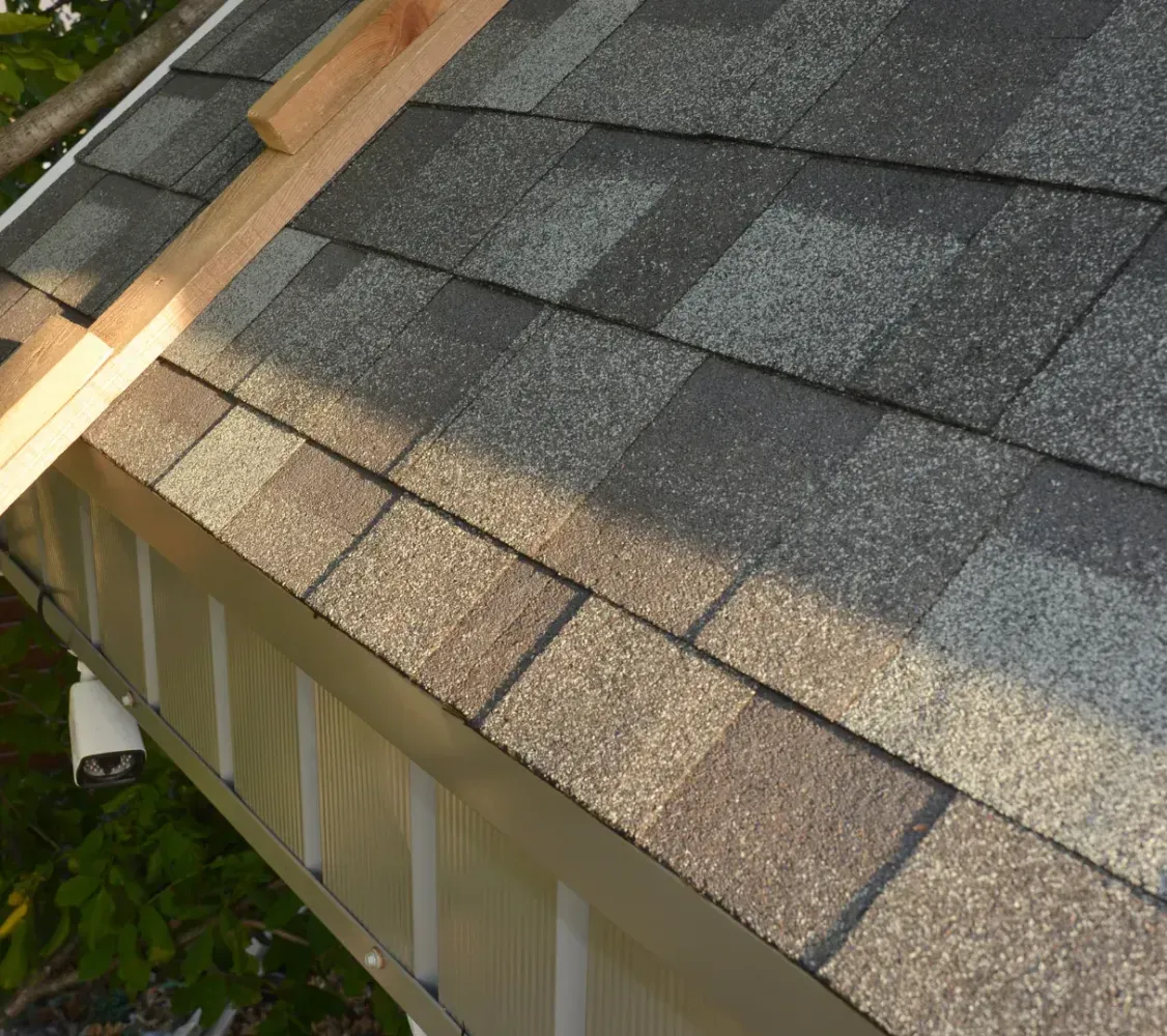 Roof shingles being installed beside a ladder on a house roof.