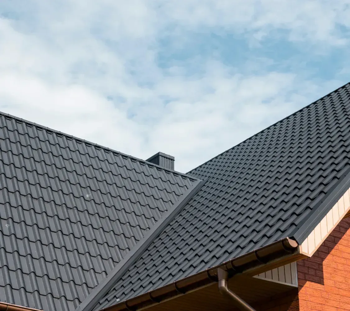 Dark gray tiled roof on a brick house against a blue sky