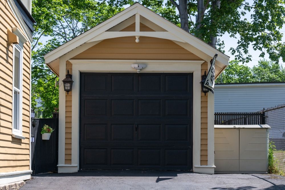 A garage with a black door is next to a house.