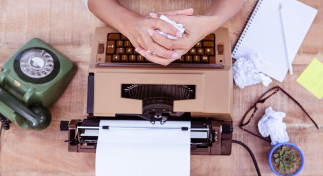 A person is typing on an old typewriter on a wooden desk.