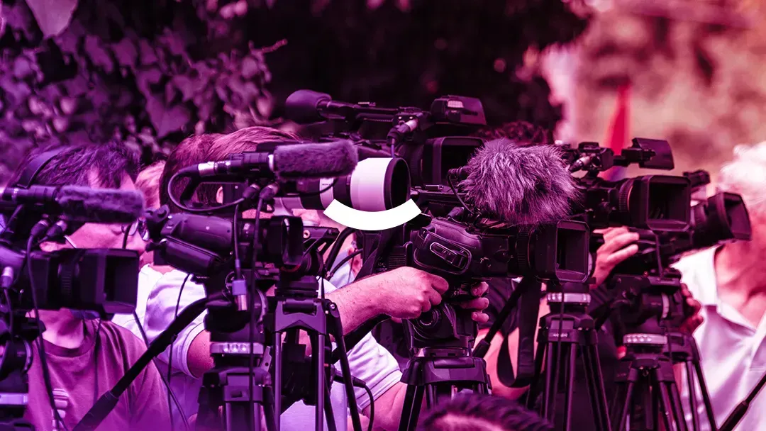 A group of people are standing in front of a row of cameras.