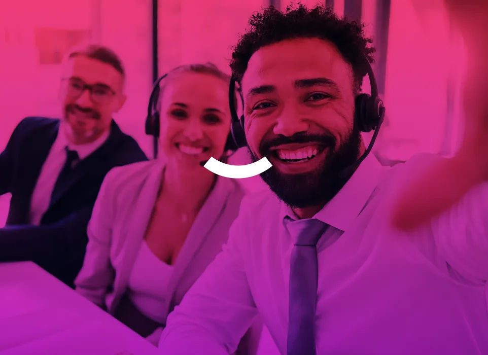 Smiling headset-wearing team member taking a selfie with colleagues in a pink-lit office