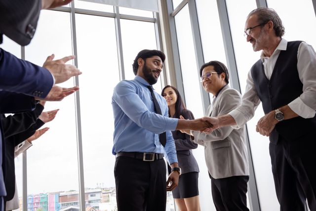 A group of business people are shaking hands in front of a window.