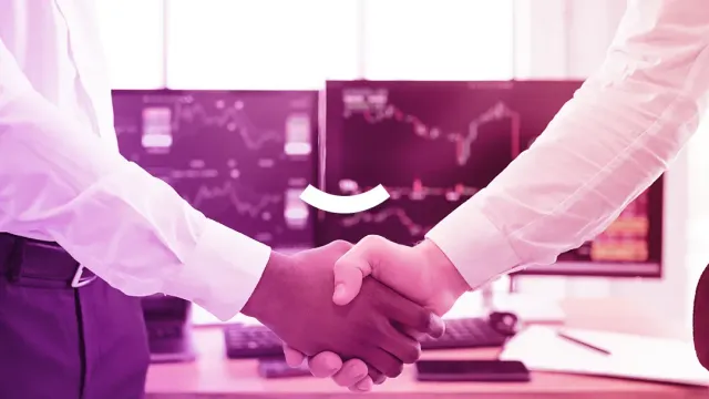 Two people are shaking hands in front of a computer screen.