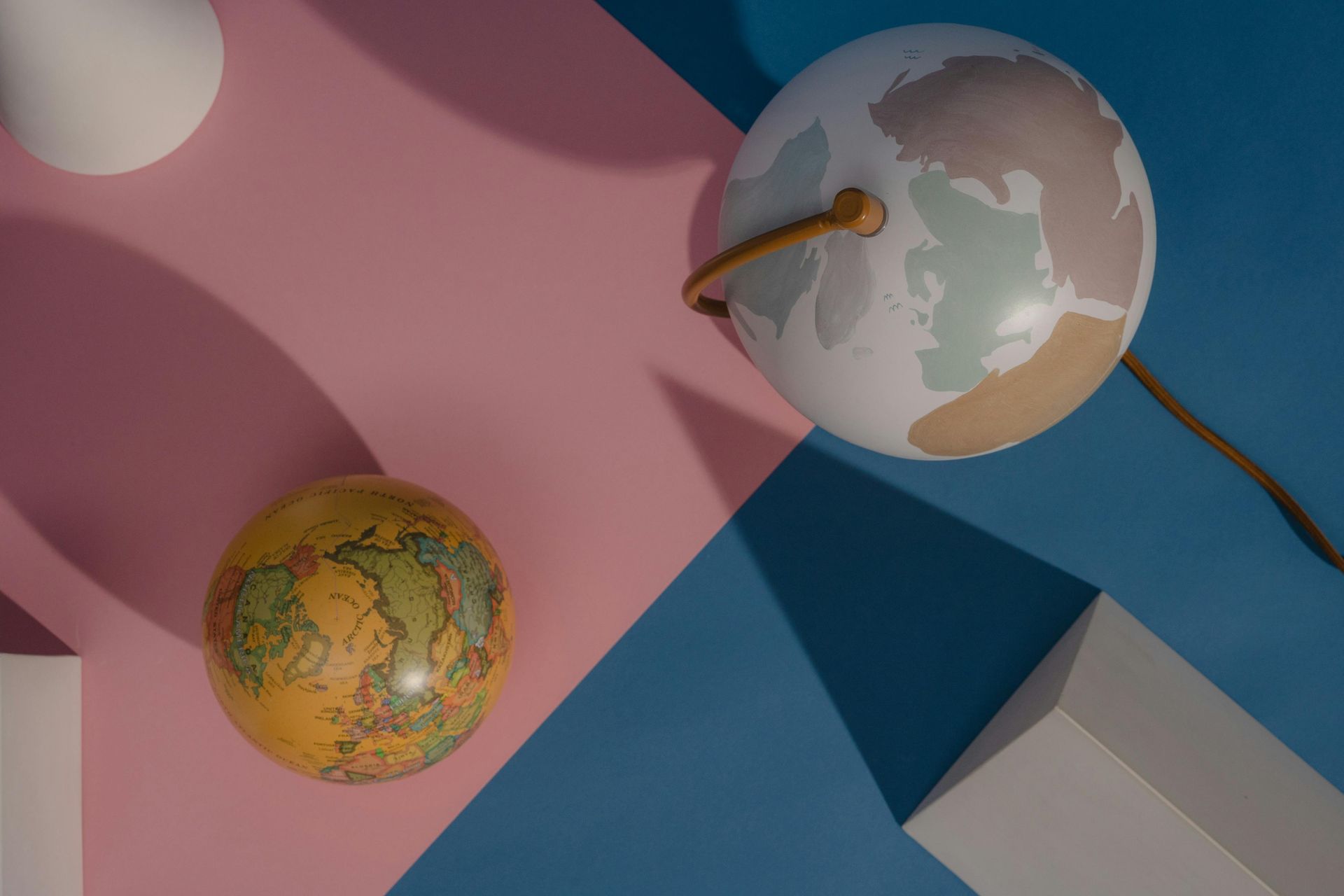 Two decorative globes on a pastel geometric wall in pink, blue, and gray.